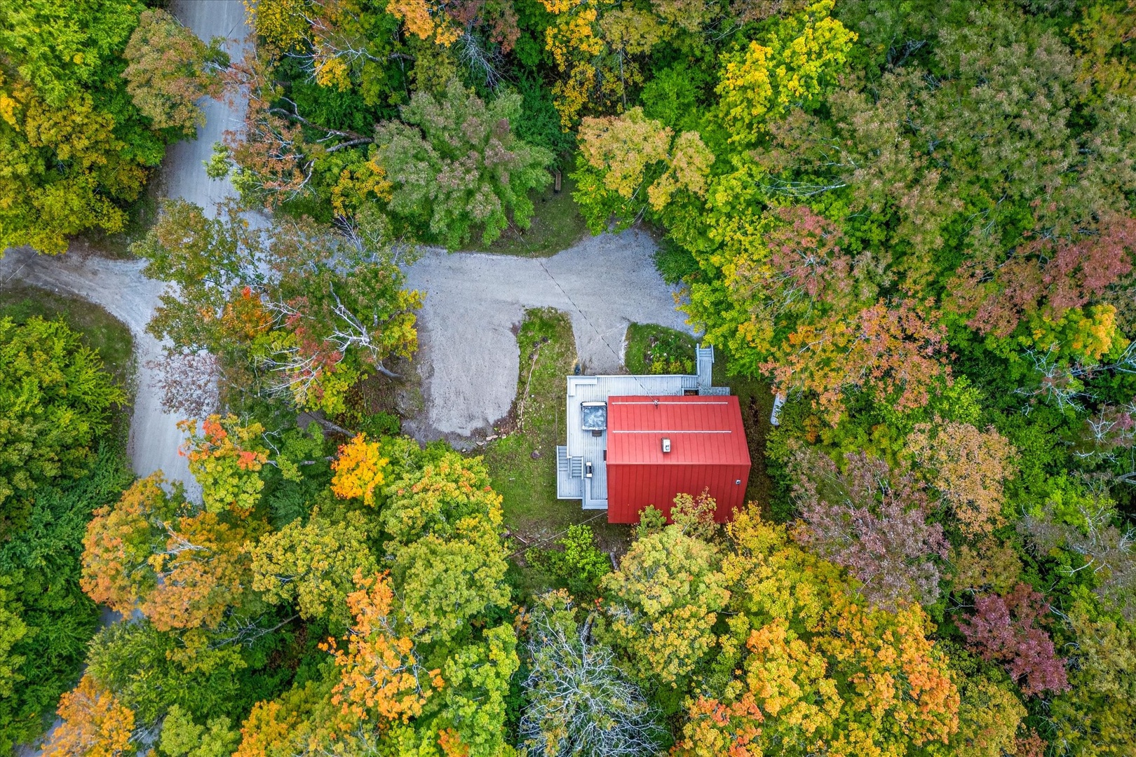 Aerial view of the property nestled among vibrant autumn foliage, with a peaceful waterfront and private access road winding through the natural landscape.