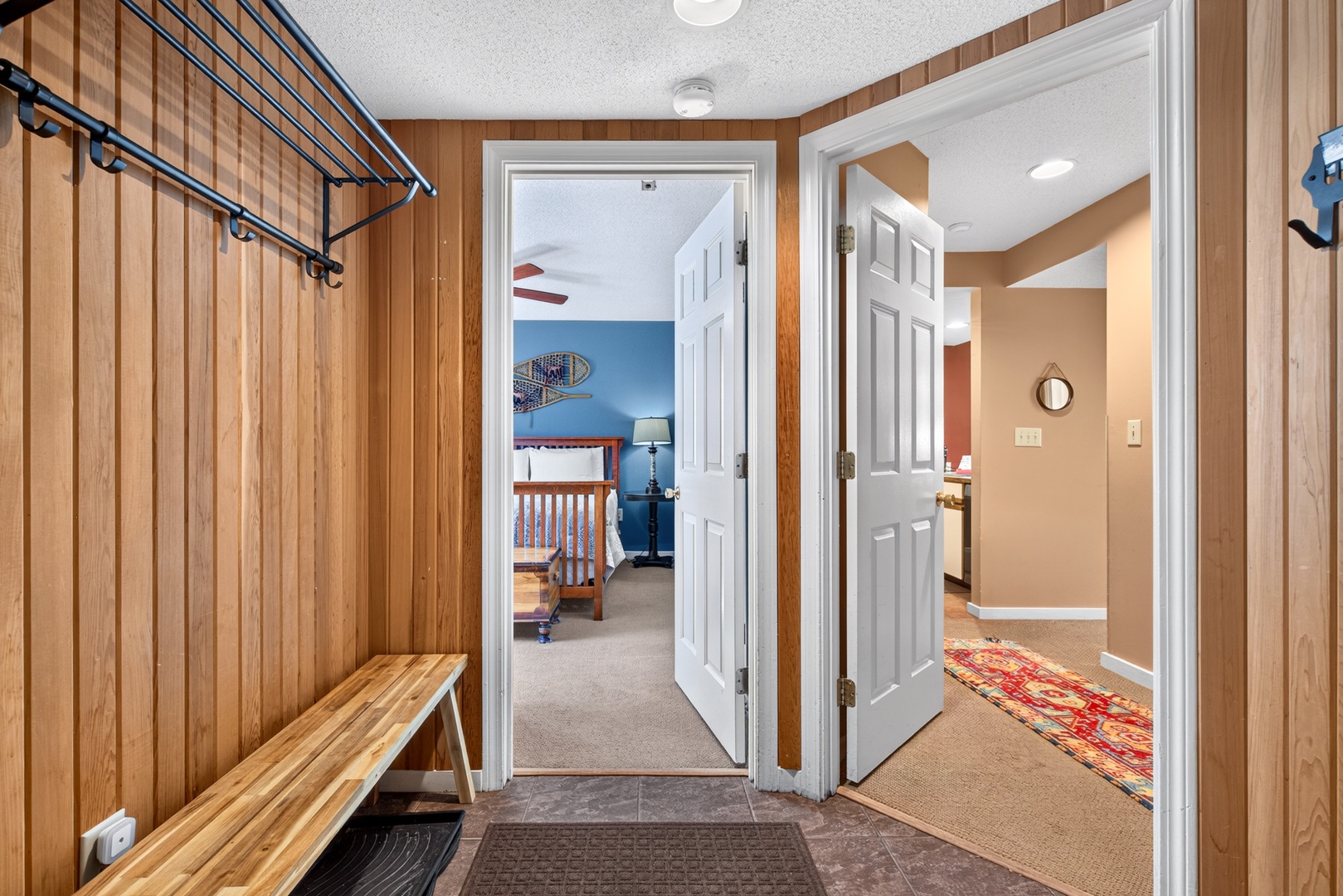 Your entryway welcomes you with warm wood-paneled walls and practical storage to keep your gear organized. Open doorways reveal cozy bedrooms and spaces beyond, ready for your group to settle in.