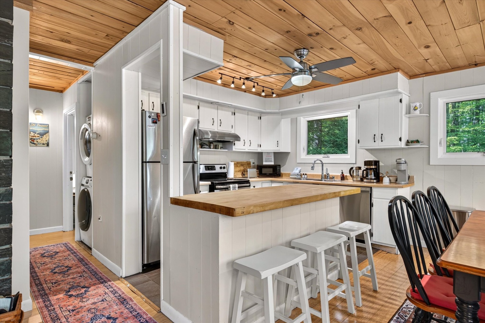 Step into your open-concept kitchen with natural wood accents and modern white cabinetry. Prep meals at the island bar, relax in the adjoining dining space, and enjoy nature views through the windows.