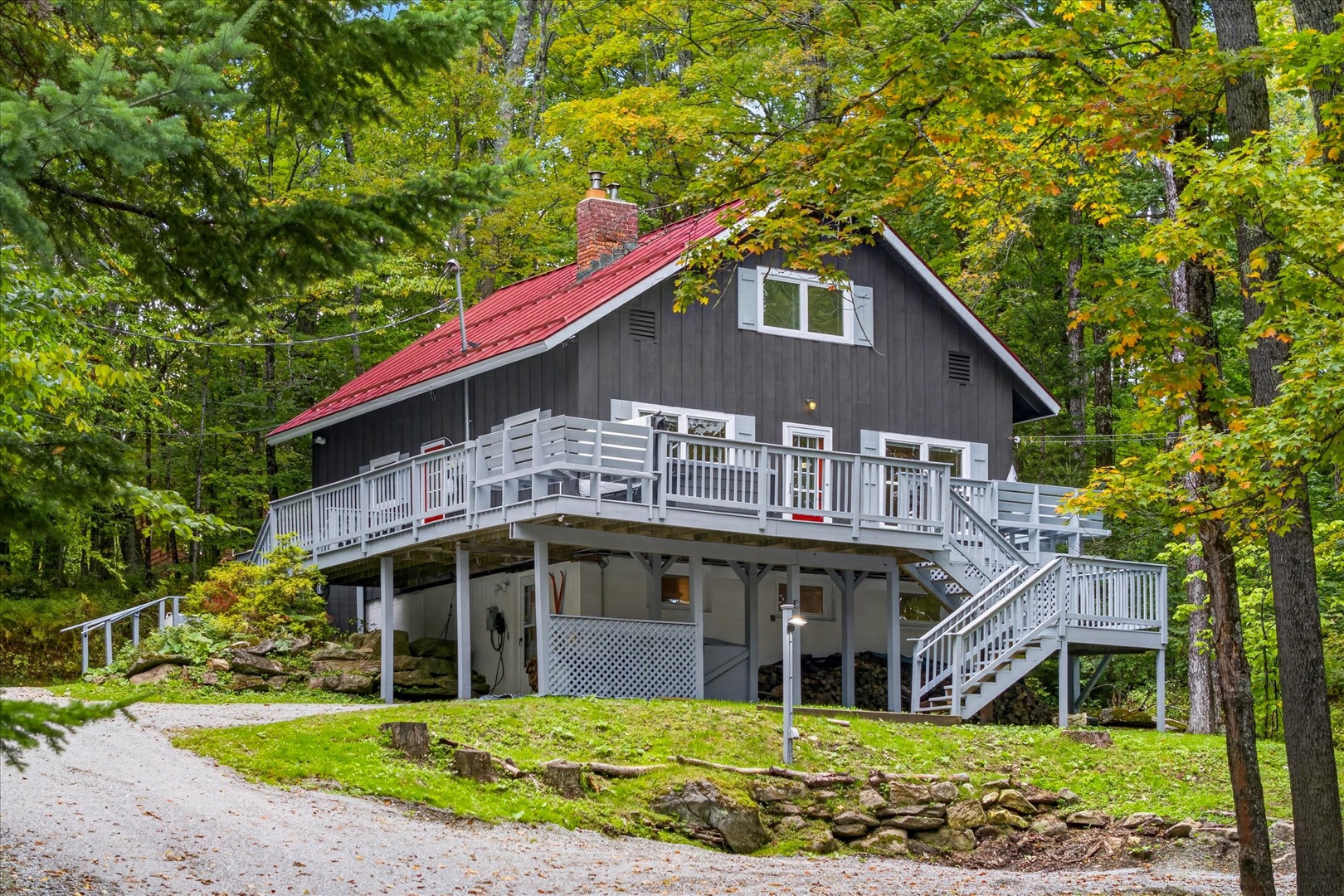 Charming two-story chalet nestled in a wooded setting, featuring a spacious wrap-around deck and vibrant fall foliage, offering peaceful seclusion surrounded by nature's beauty.