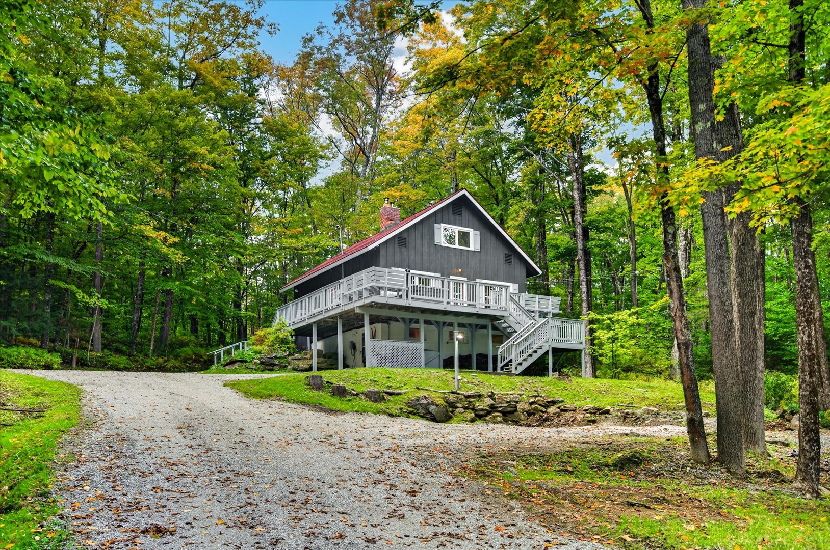 A charming mountain retreat nestled among vibrant trees, with a welcoming wrap-around deck and peaceful forested surroundings.