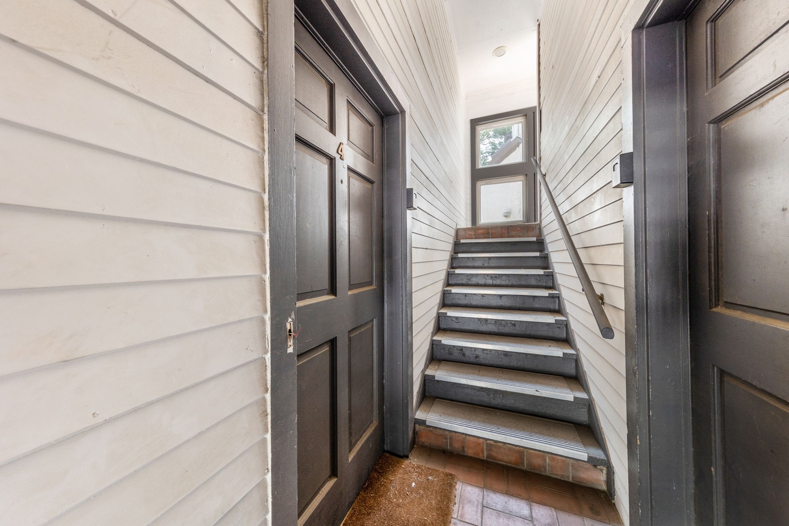 The property features a private exterior stairwell with classic architectural details, including paneled doors and horizontal wood siding painted in neutral tones.