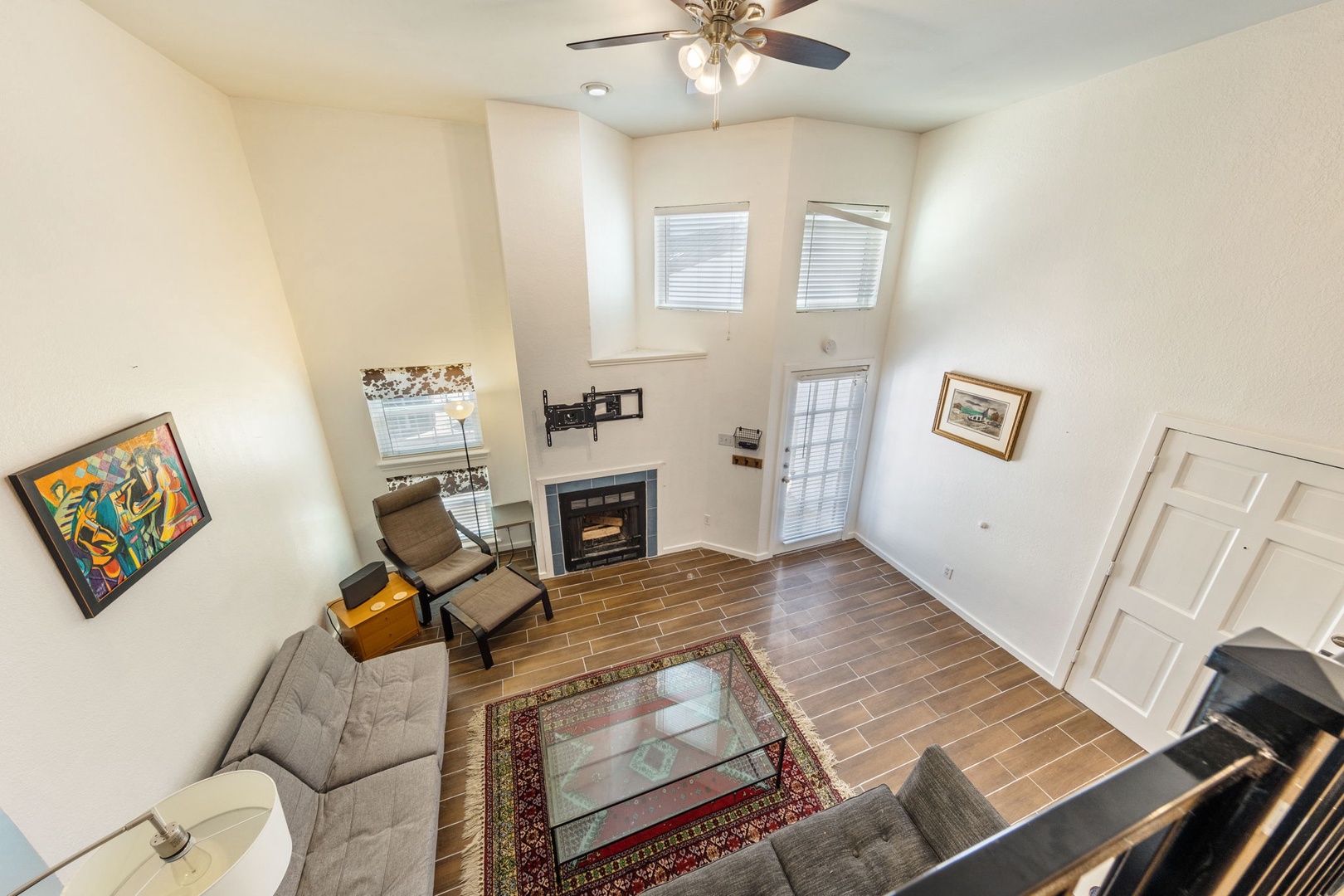 TV currently installed above fireplace not shown.  Relax in your spacious living room with warm wood-look floors, cozy fireplace, and ceiling fan. Natural light streams through multiple windows while you unwind on the comfortable seating.