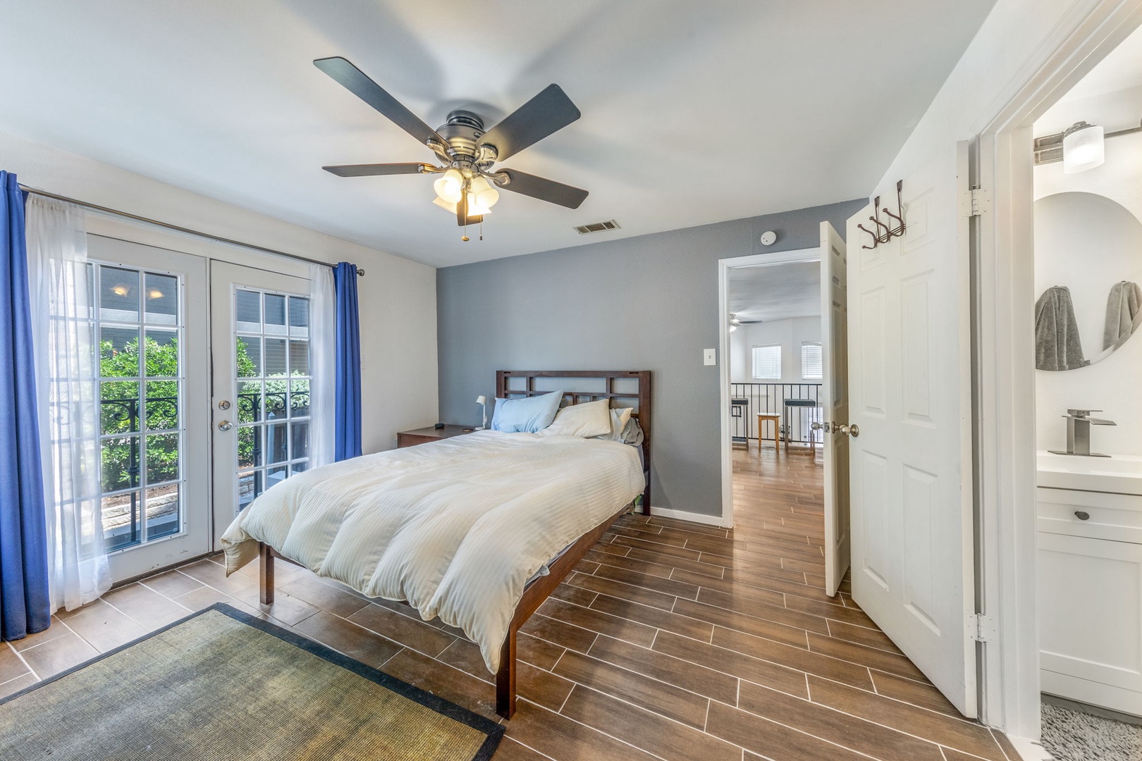 Relax in your spacious bedroom with a plush bed, natural light streaming through French doors, and a cooling ceiling fan overhead. The ensuite bathroom and warm wood-look floors complete your private retreat.