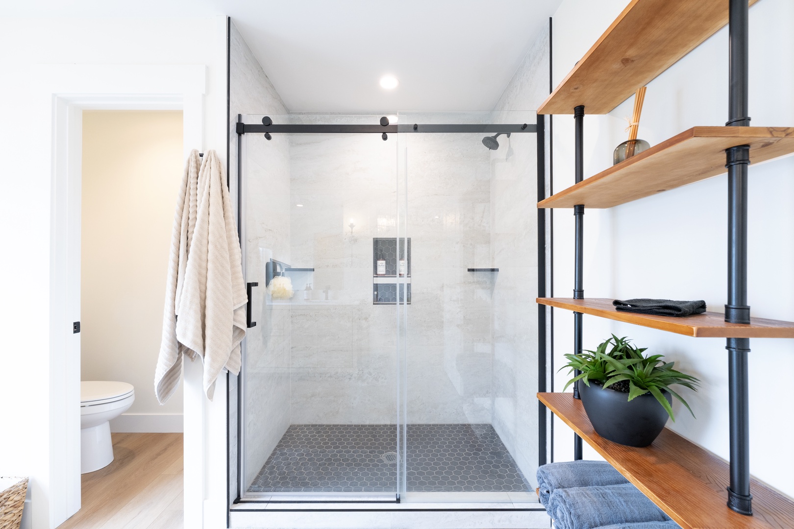 Step into your modern spa-like retreat, where sleek black-framed glass and warm wood shelving create a serene, stylish bathroom oasis just for you.