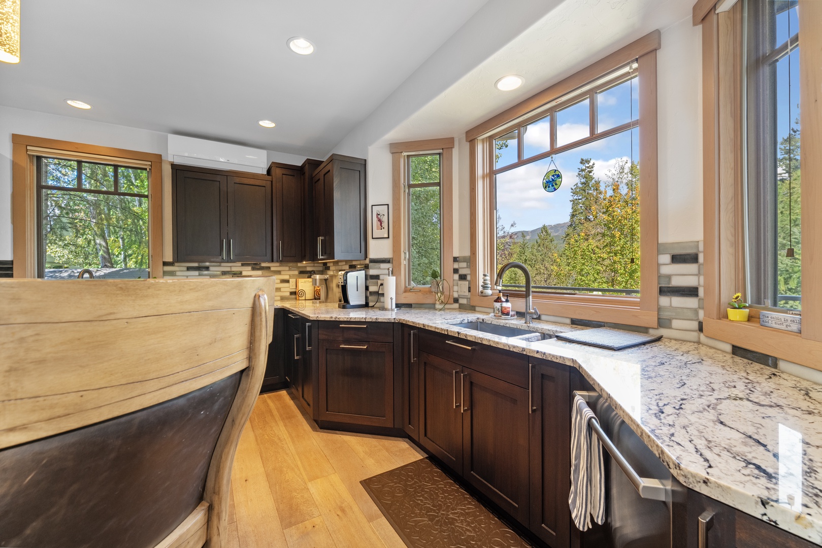 Picture yourself preparing meals in this bright, modern kitchen with stunning mountain views through large windows, rich wood cabinetry, and beautiful granite counters—your perfect retreat for mountain living.