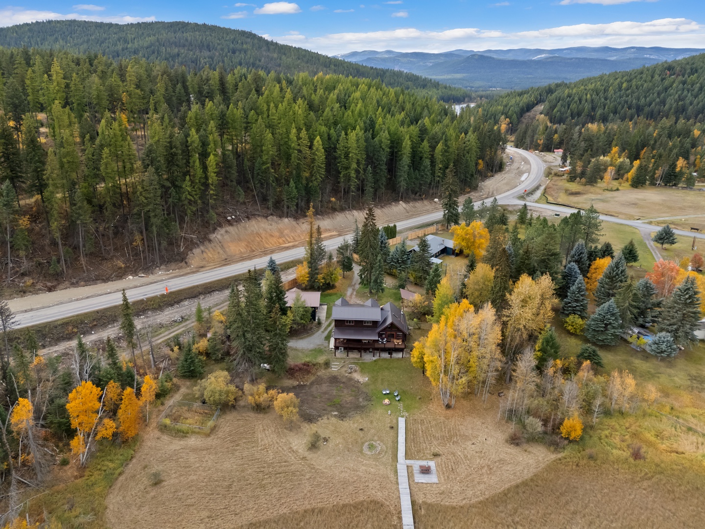 Aerial view of property nestled in autumn forest valley with golden foliage and mountain backdrop.