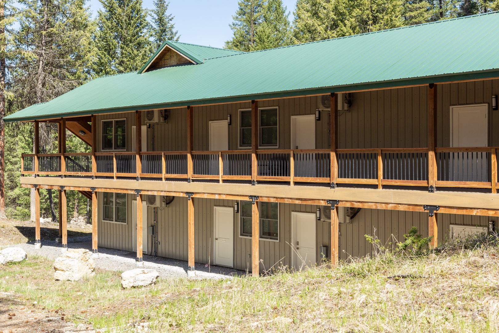 A mountain retreat with expansive wraparound deck showcasing two-story lodging nestled among towering evergreens, offering serene forest surroundings and outdoor relaxation spaces.