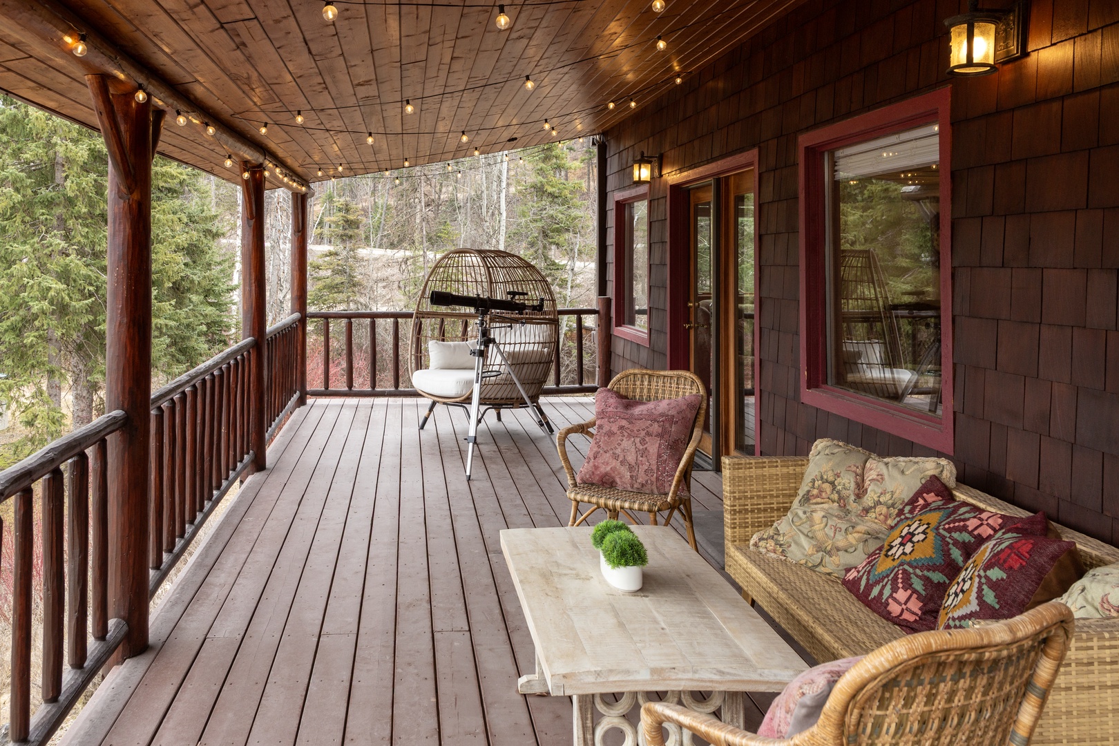 Unwind on your private covered deck with wicker seating, twinkling lights overhead, and peaceful forest views stretching beyond the railing.
