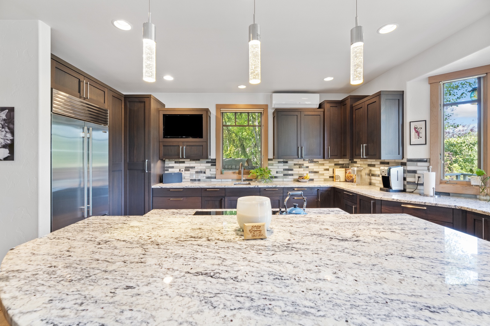 Your gourmet kitchen awaits with gleaming granite counters, modern pendant lighting, and rich wood cabinetry. Sunshine pours through large windows while you prepare meals surrounded by high-end appliances and mountain views.