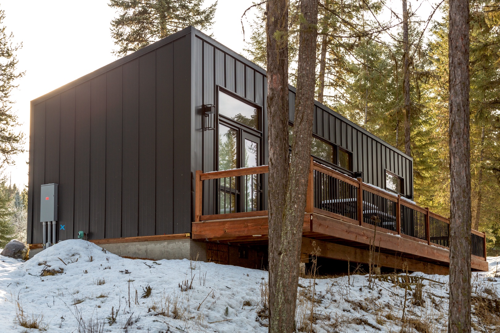 Modern mountain retreat nestled among towering pines with a spacious wooden deck, offering a peaceful winter escape surrounded by pristine forest.