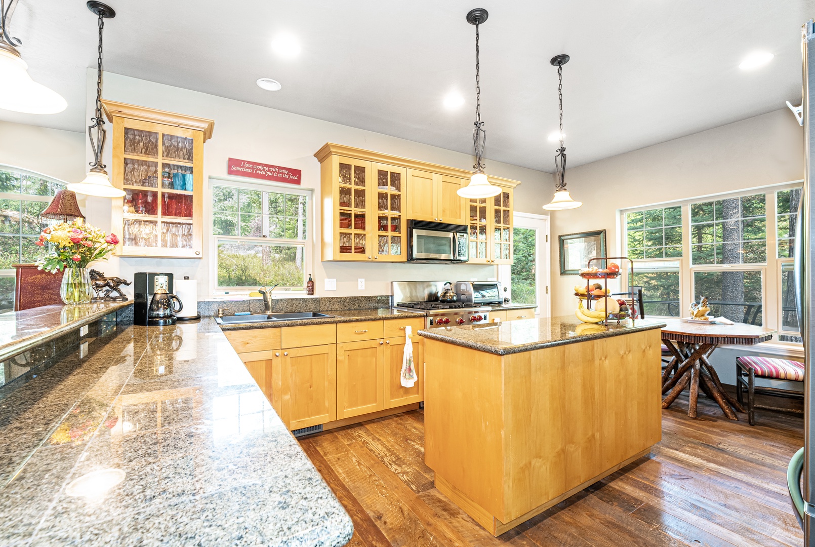 A bright, open kitchen where you'll love preparing your meals, with gleaming granite counters, warm wood cabinetry, and a spacious island for gathering. Large windows frame leafy views and fill the room with natural light.