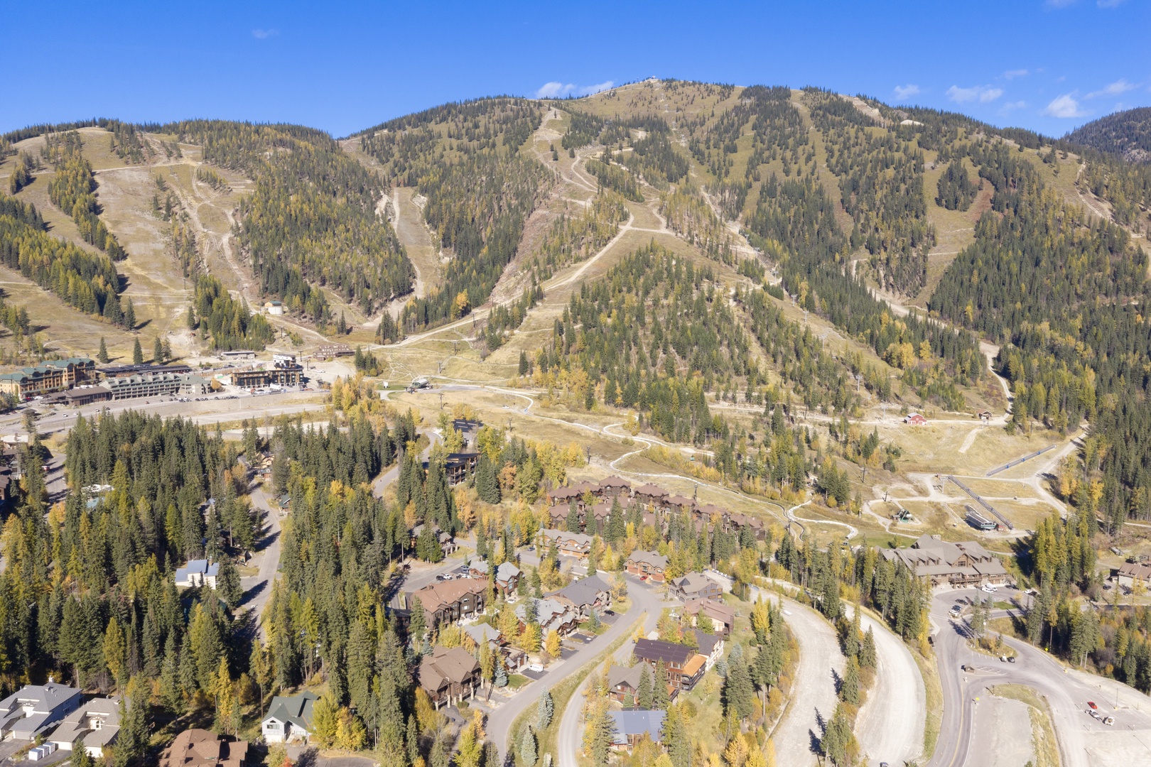 An aerial view captures the property nestled in a forested mountain valley with ski slopes and seasonal foliage surrounding the area.