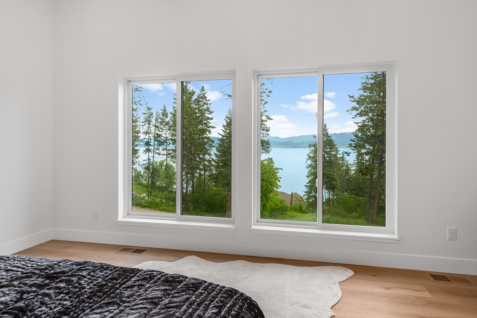 Wake up to serene lake views through floor-to-ceiling windows, where evergreens frame tranquil waters and distant mountains—your peaceful escape awaits.