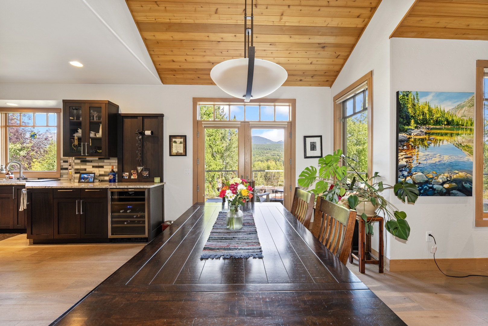 Gather around the handcrafted dining table under warm wood ceilings, where windows frame stunning mountain vistas and your kitchen awaits nearby.