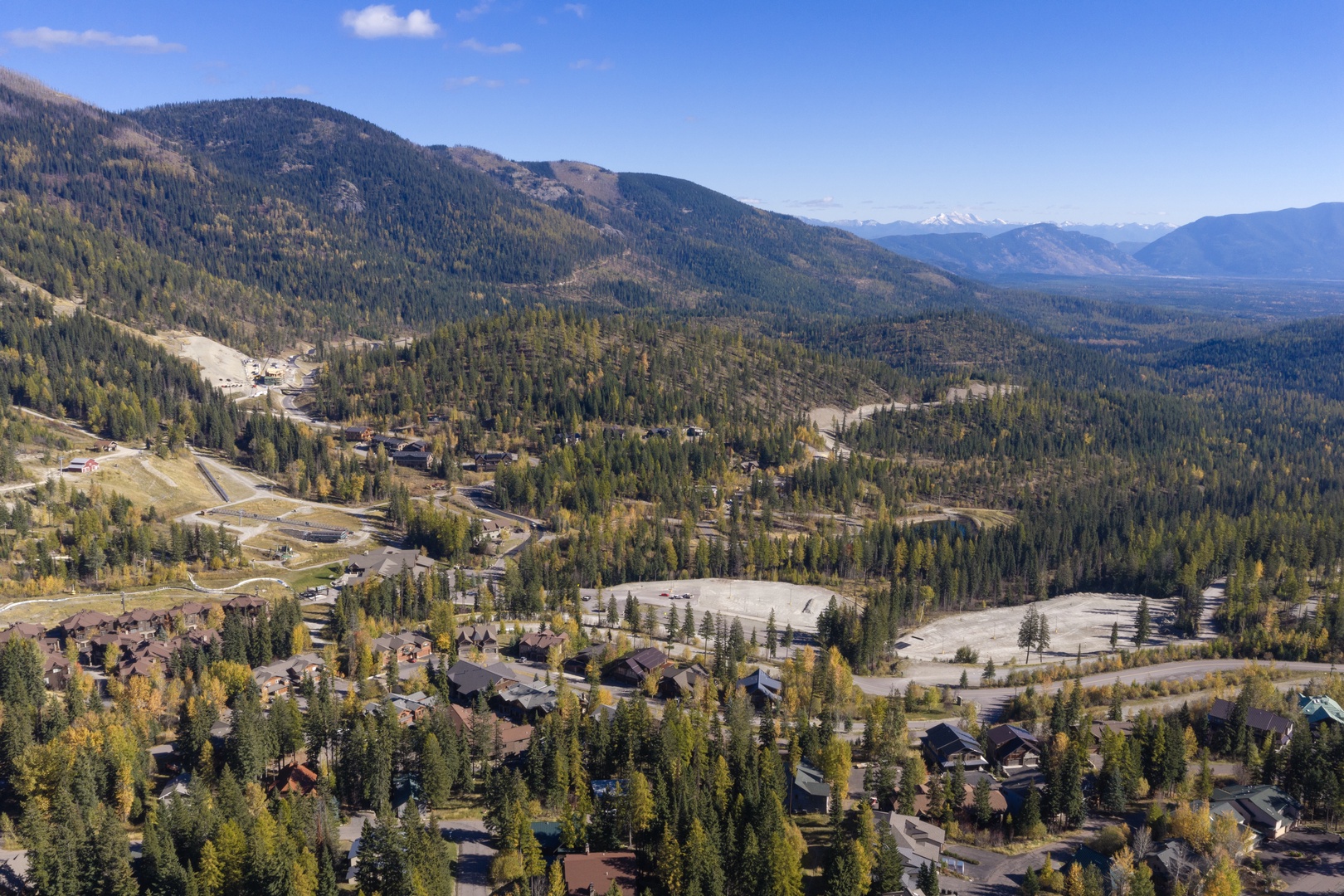 Aerial view capturing the property nestled among evergreens and mountain terrain, with autumn colors and distant peaks marking the surrounding wilderness area.