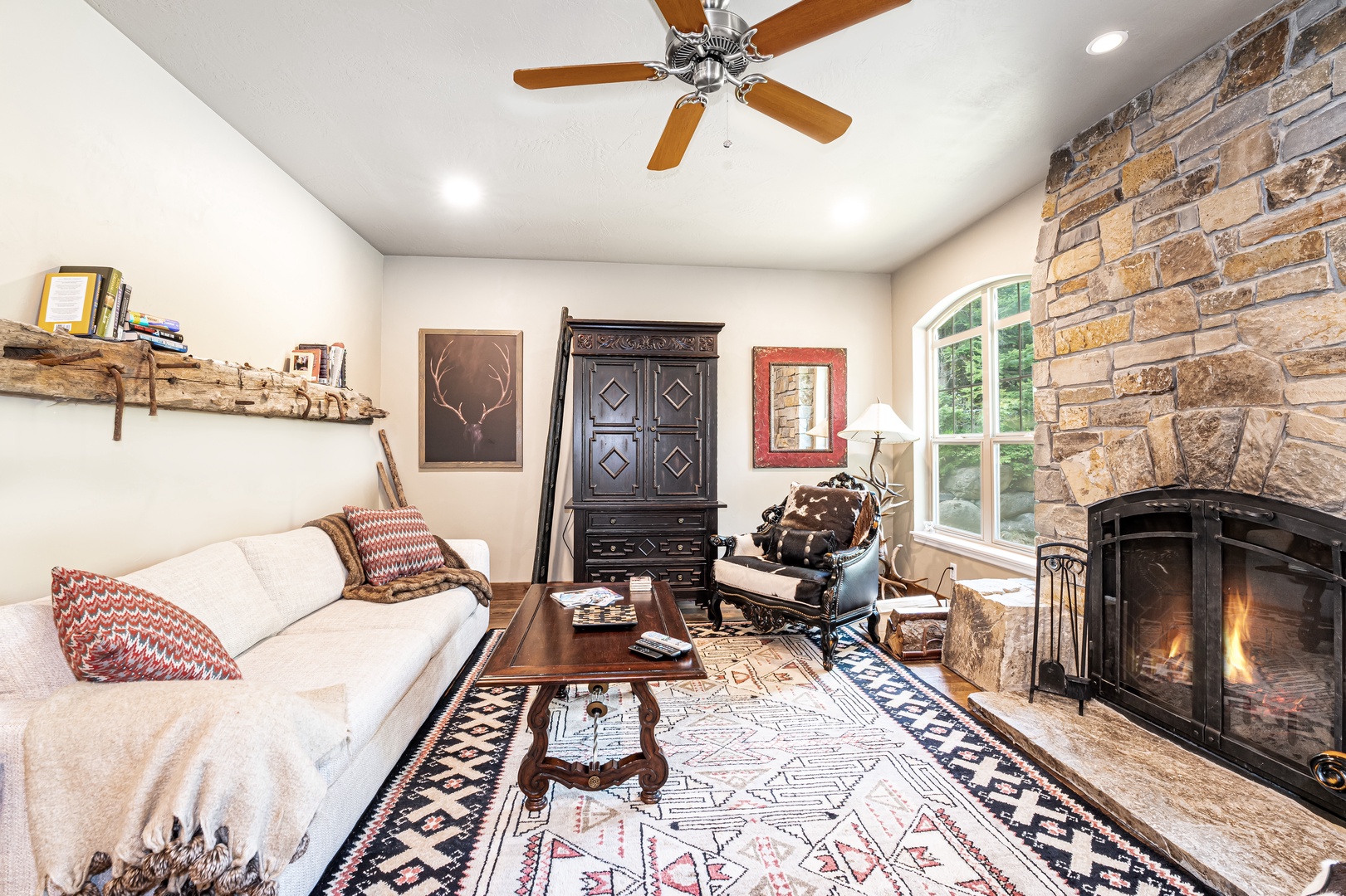 Settle into your cozy living space where rustic charm meets modern comfort, featuring a warming fireplace, vaulted ceilings with a ceiling fan, and natural light flooding through large windows—perfect for unwinding after a day of adventure.