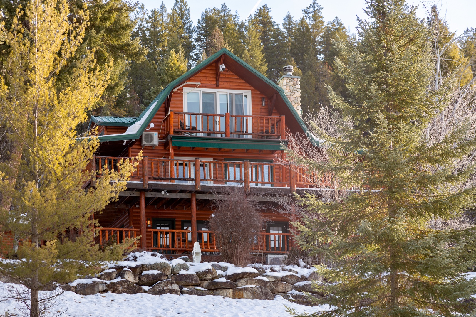 A charming log cabin nestled among evergreens and aspens, offering a peaceful mountain retreat with multiple decks and a cozy stone chimney.
