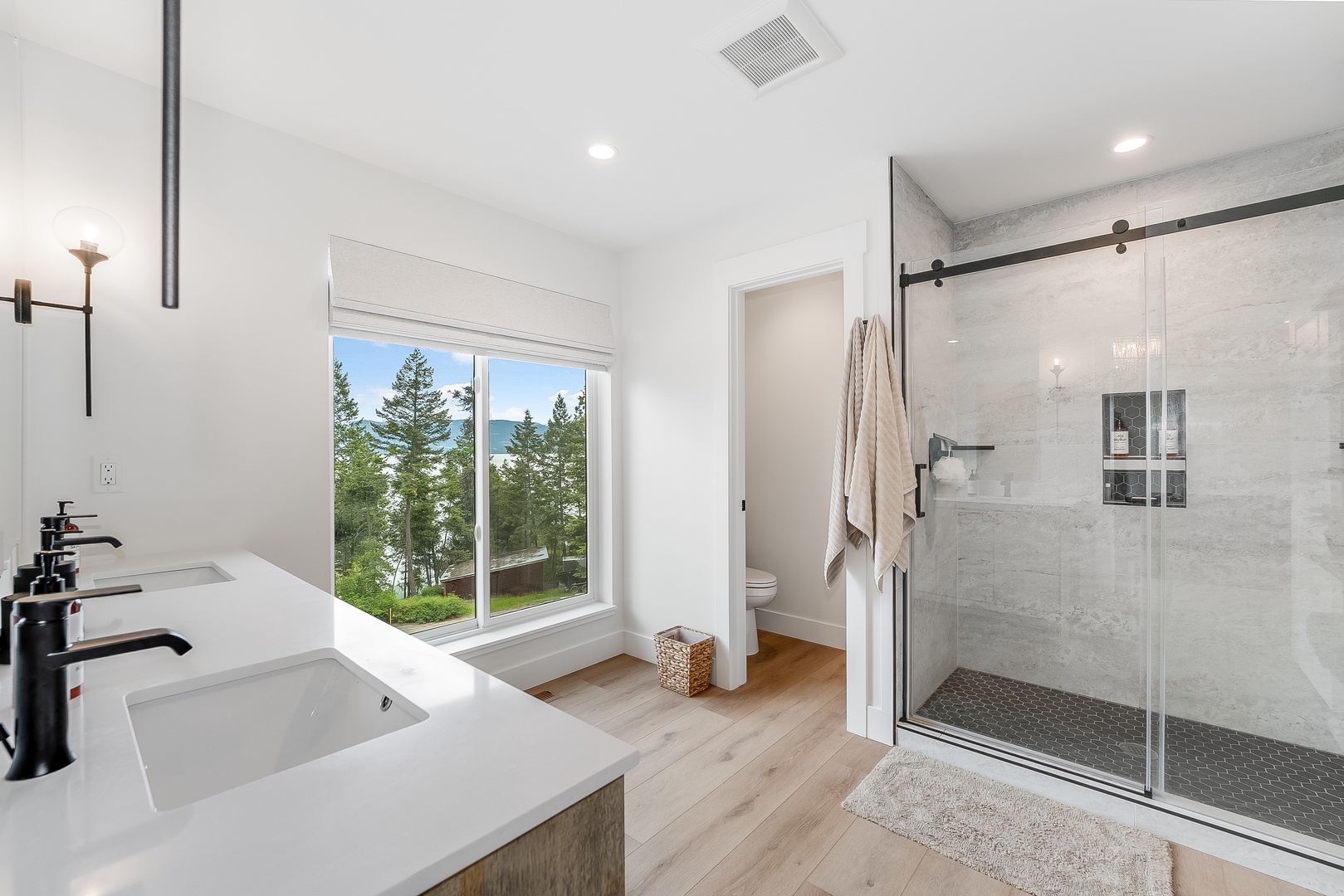 Step into your serene private bathroom where sleek modern design meets breathtaking natural views. Refresh in the spacious walk-in shower, then gaze out at towering evergreens and shimmering water beyond.