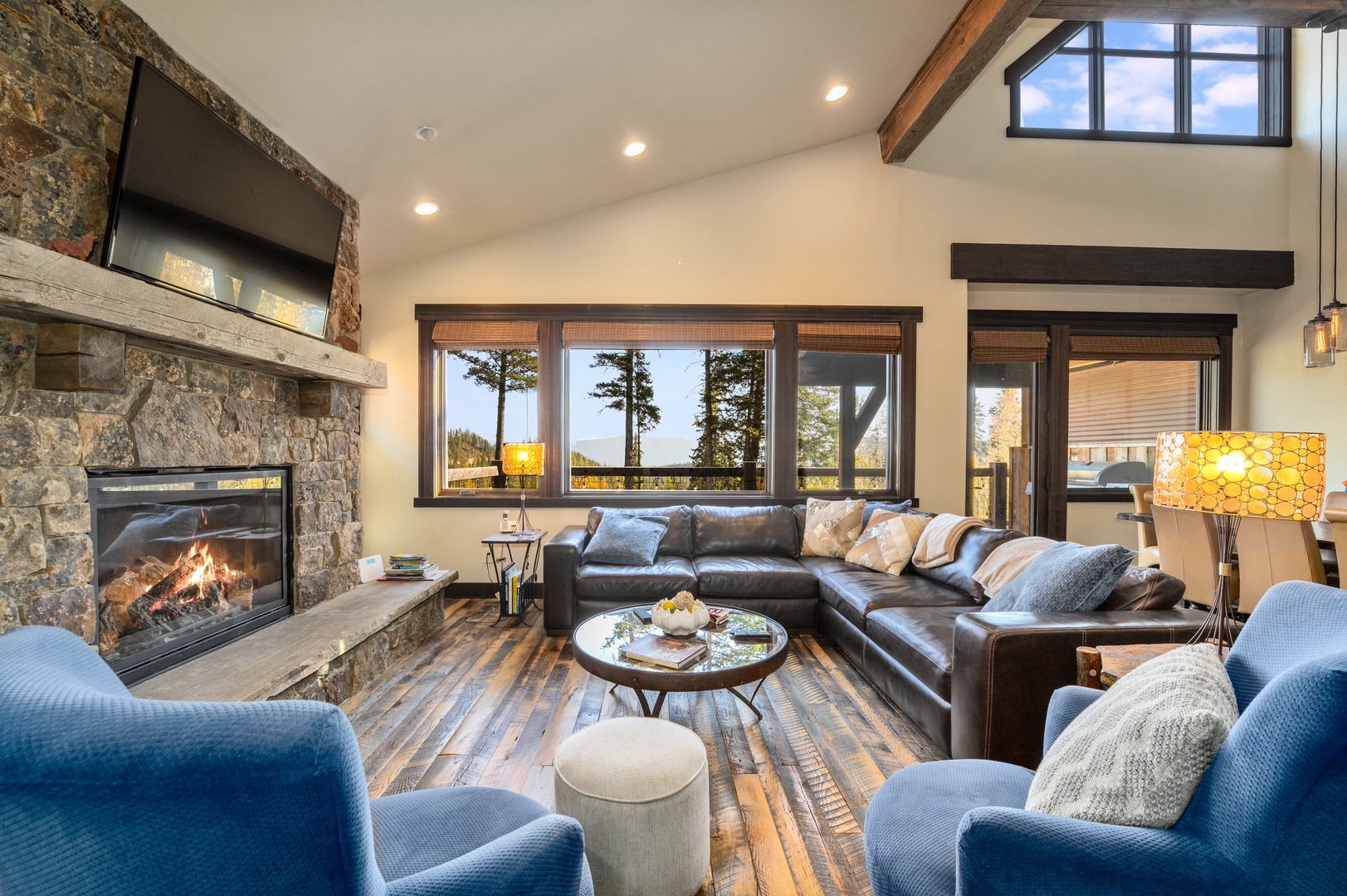 Settle into your inviting living space where a crackling stone fireplace and plush seating create the perfect retreat. Tall windows frame tranquil forest views, filling the room with natural light and mountain-home charm.