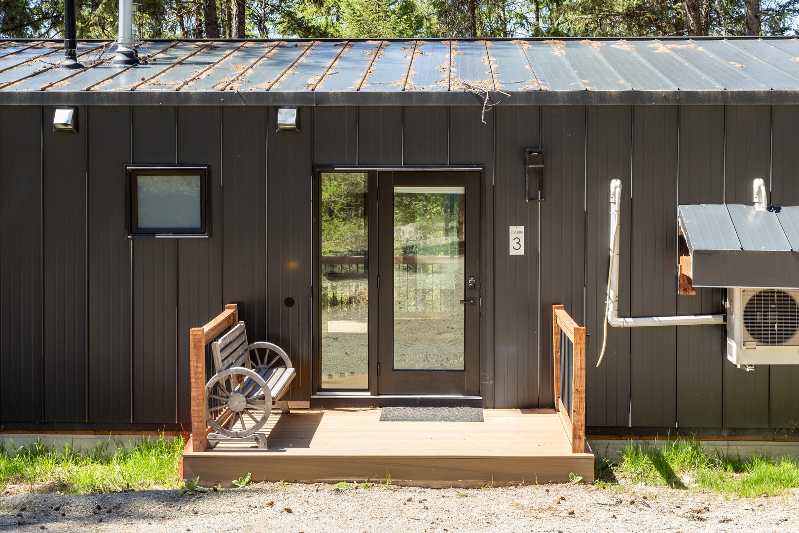 The charming entrance to unit 3 features a cozy wooden porch with a rustic wagon-wheel bench, nestled in a peaceful wooded setting.