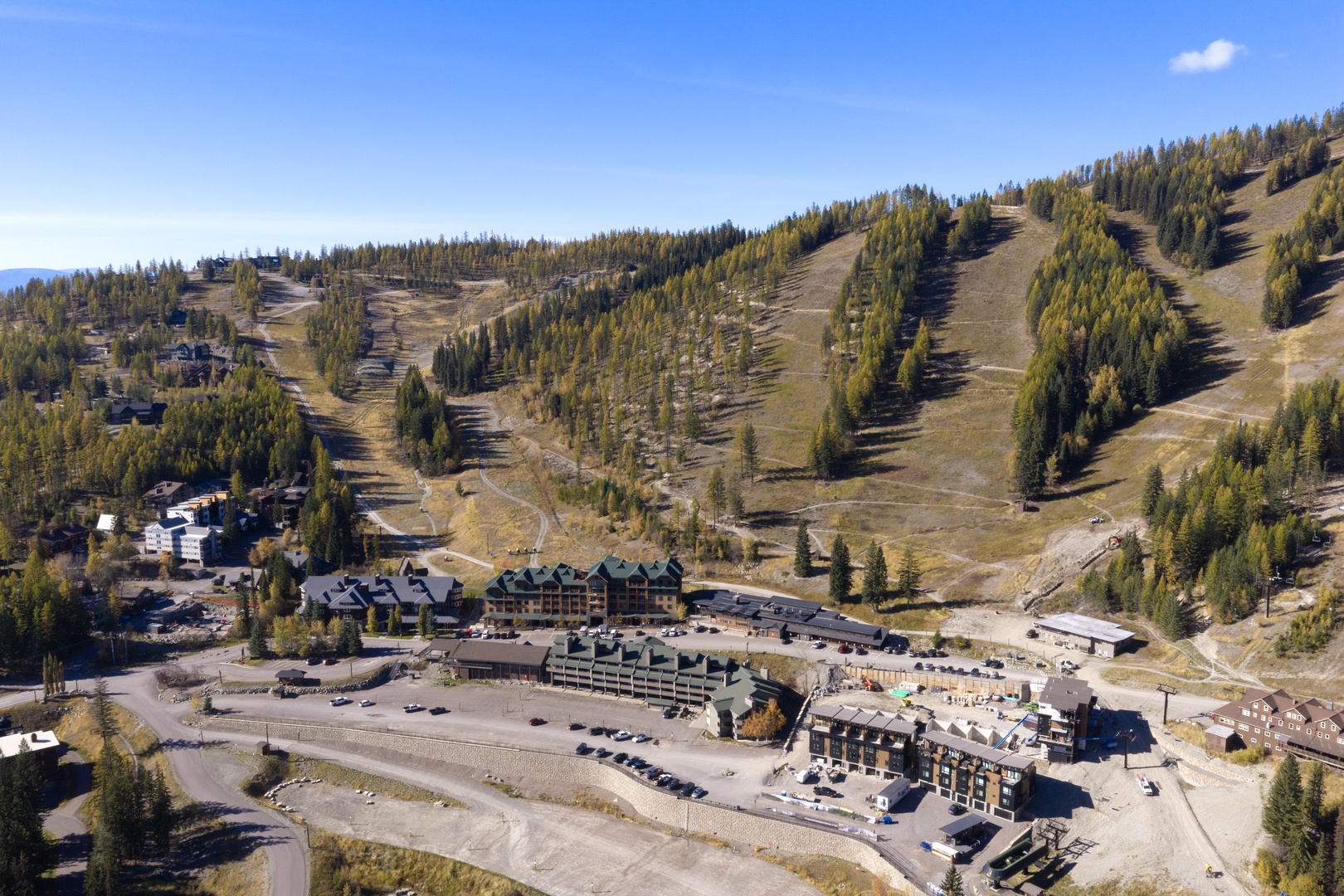 Aerial view of the property nestled at the base of ski slopes, surrounded by forested mountain terrain and seasonal outdoor beauty.