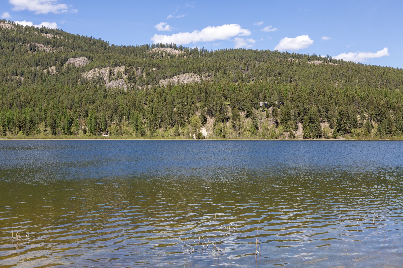 A pristine lake surrounded by dense evergreen forest and dramatic rocky outcrops beneath a clear blue sky, offering a peaceful natural setting near the property.