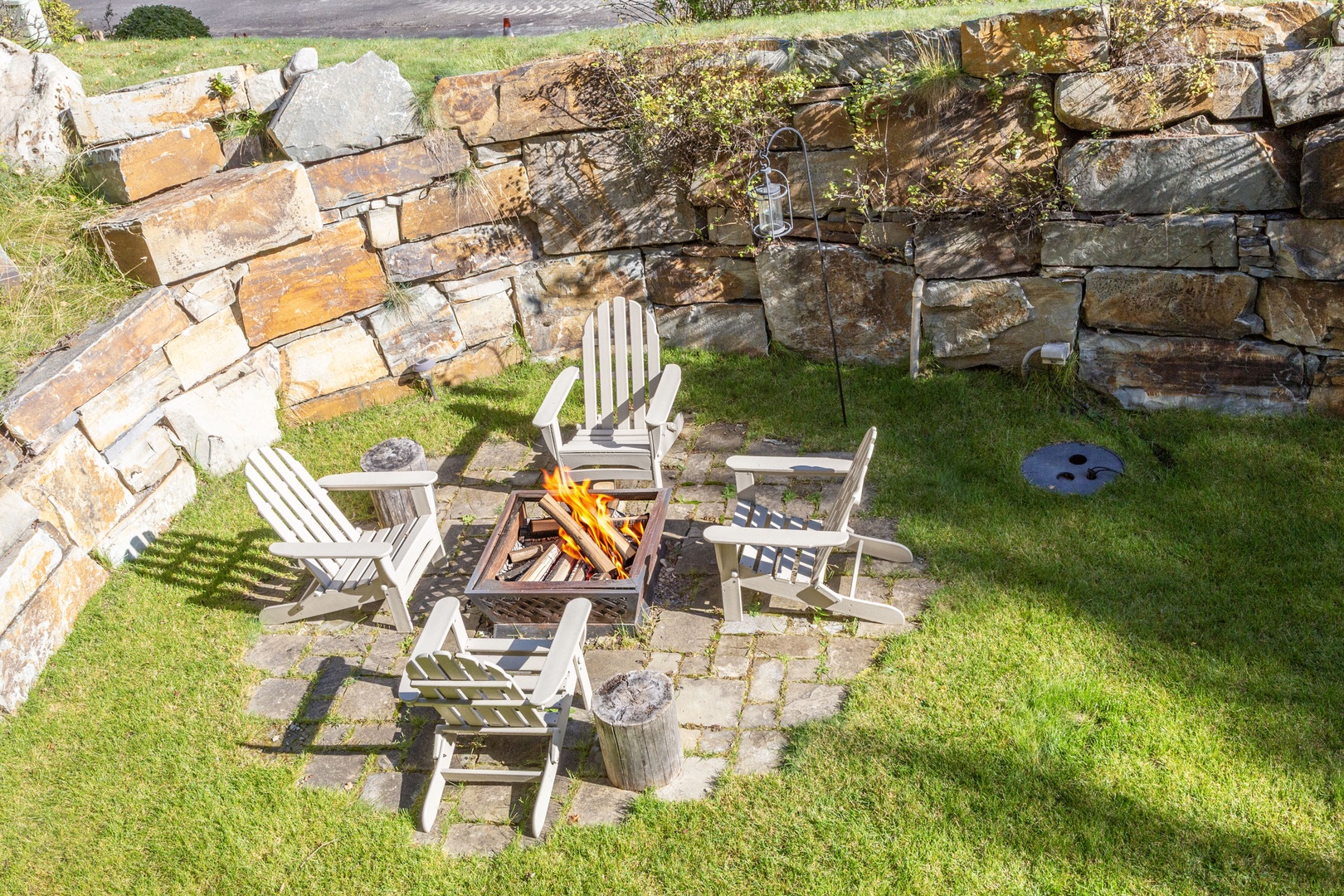 Aerial view of the rustic stone-walled patio area featuring a fire pit surrounded by Adirondack chairs, perfect for relaxing evenings outdoors.