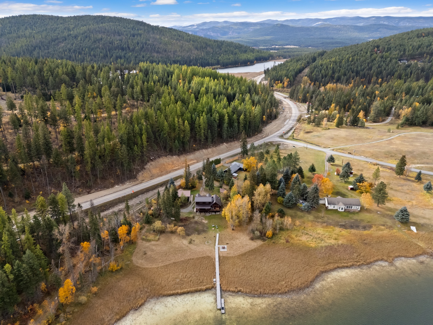 Stunning aerial view showcases the property nestled among forested hills and lakefront, with vibrant autumn colors painting the landscape.