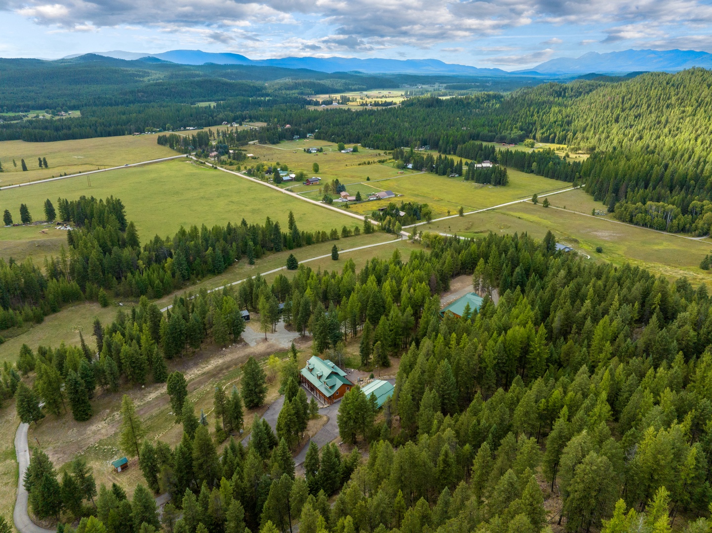 Aerial view showcases the property nestled among pristine forests with rolling valleys and distant mountain ranges creating a stunning rural landscape.