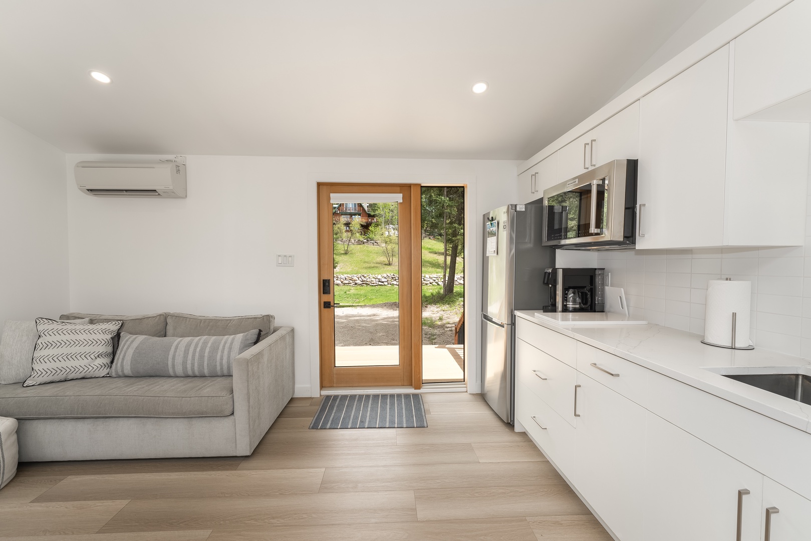 Your modern open-plan retreat combines living and kitchen spaces with sleek finishes, welcoming natural light through garden-view glass doors, and climate comfort at your fingertips.