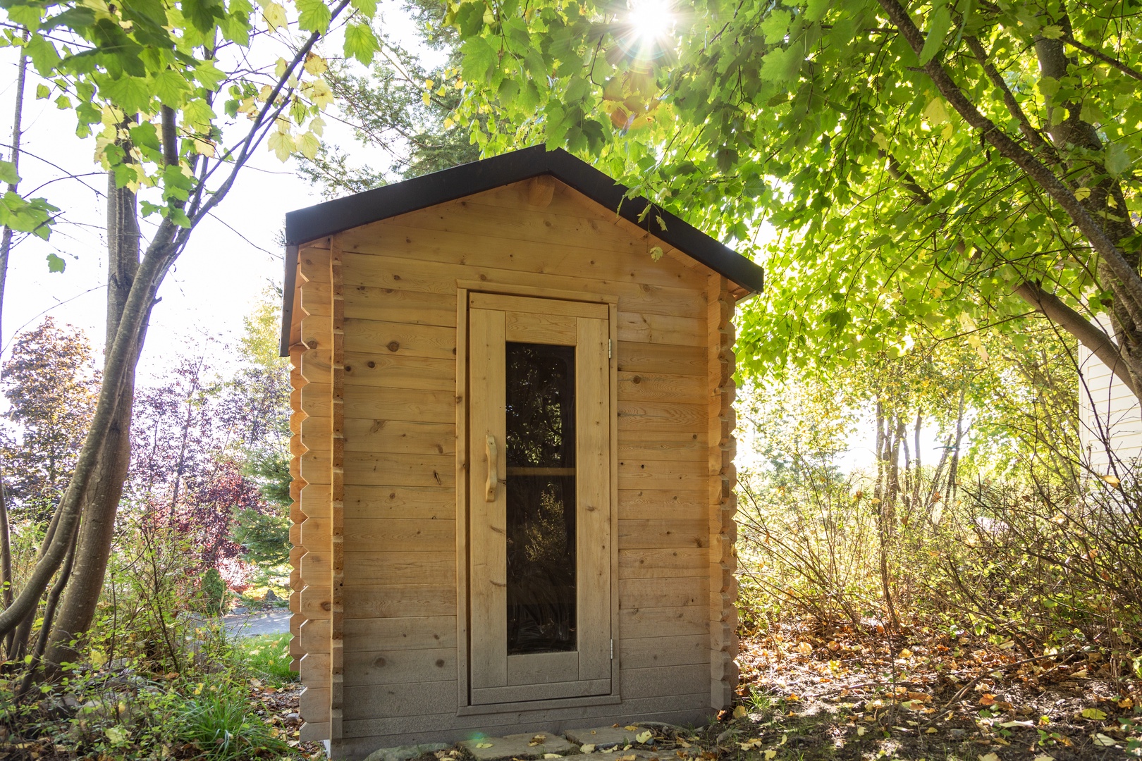 A charming wooden cabin nestled beneath dappled sunlight and vibrant green foliage, offering a tranquil escape in a natural, garden-like setting.