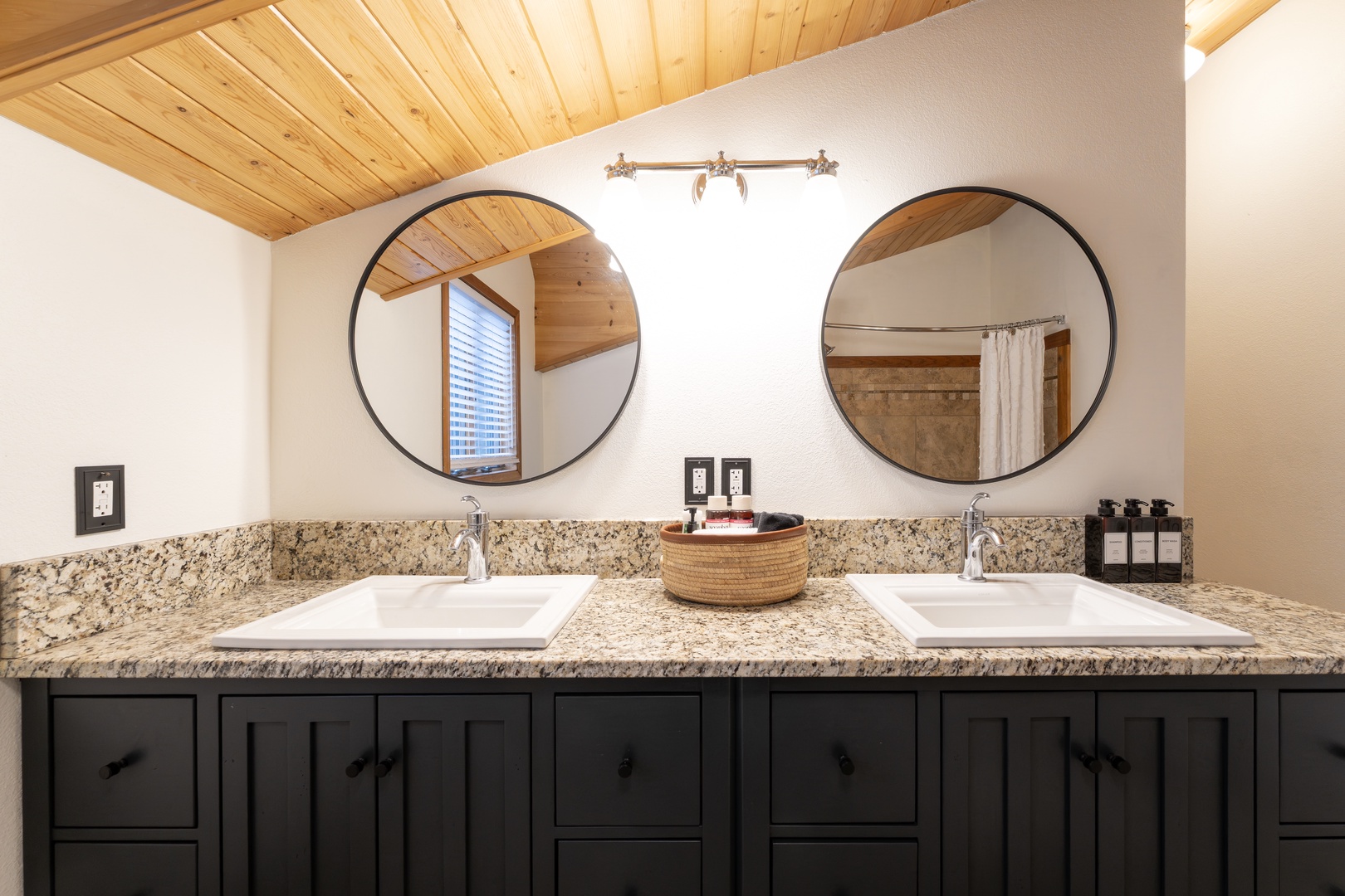 Your ensuite features dual vanities with granite countertops and stylish round mirrors under warm wood beam ceilings.