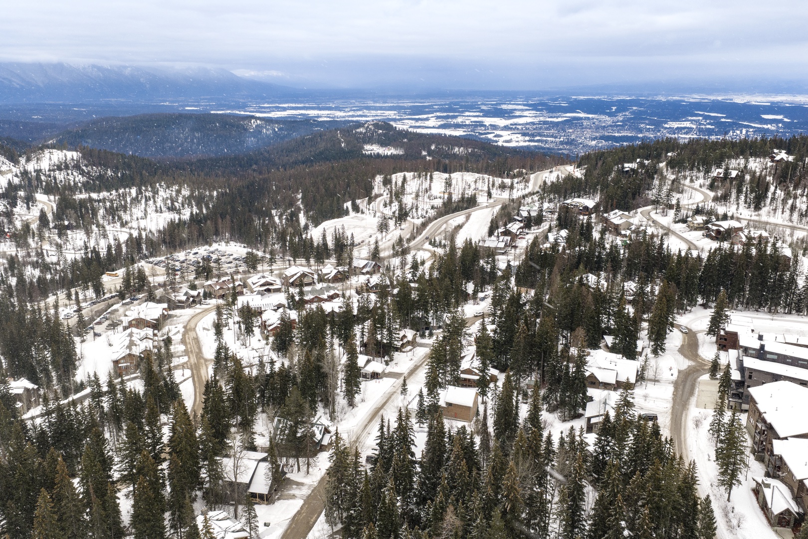 Aerial view of a winter ski resort nestled in snow-covered mountains with ski slopes and forest terrain stretching across the valley.