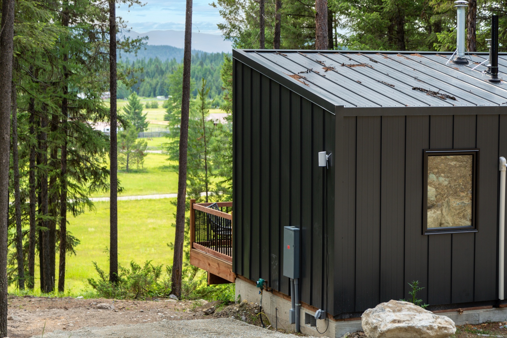 Cozy forest cabin with panoramic views of rolling green valleys and distant mountains through towering pine trees.
