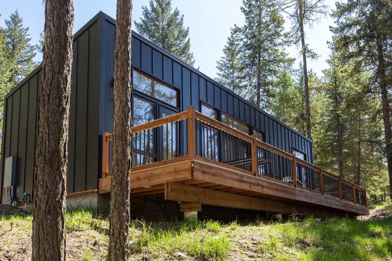 Modern cabin nestled among towering pines, featuring a wrap-around wooden deck—perfect for sipping morning coffee surrounded by nature's peaceful beauty.