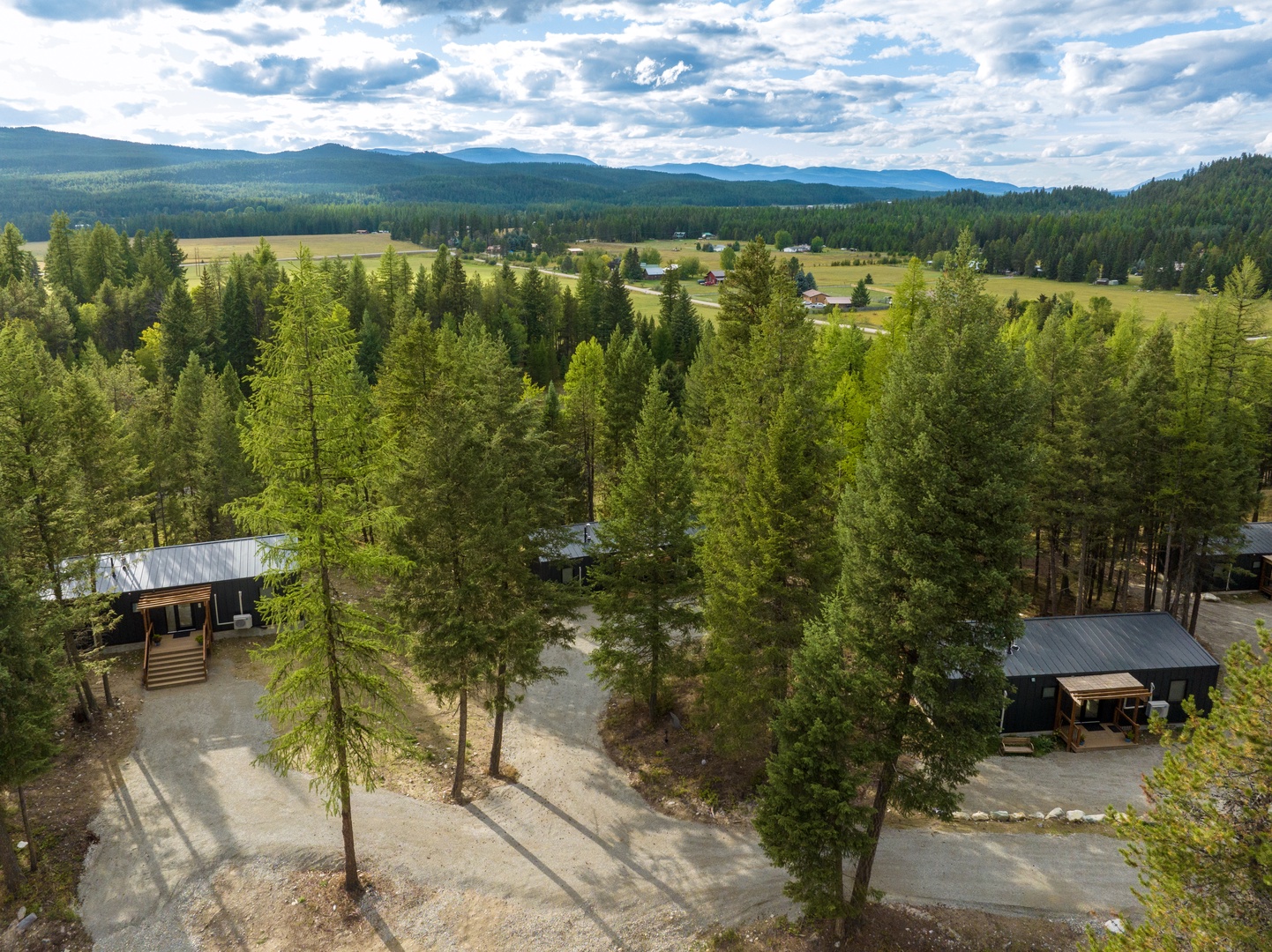Aerial view of a peaceful vacation rental property nestled among towering pines, with mountain vistas and open meadows framing this serene woodland retreat.