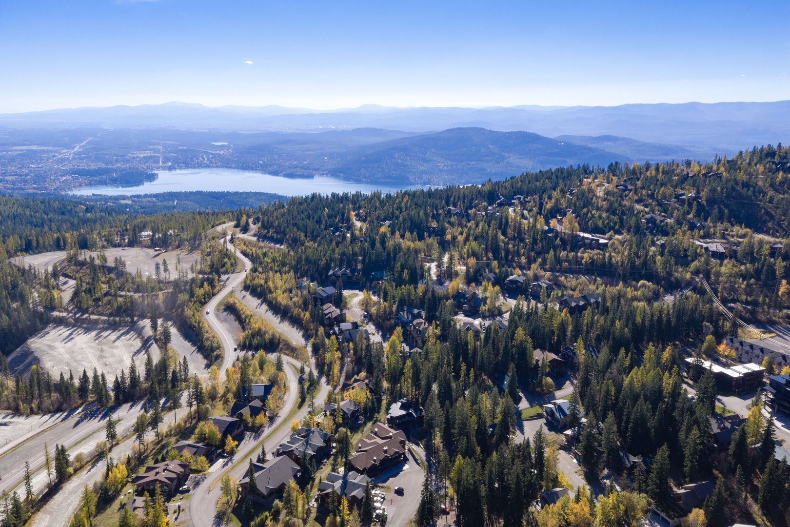 An aerial perspective showcases the property's forested mountain setting with sweeping lake and distant mountain vistas in every direction.