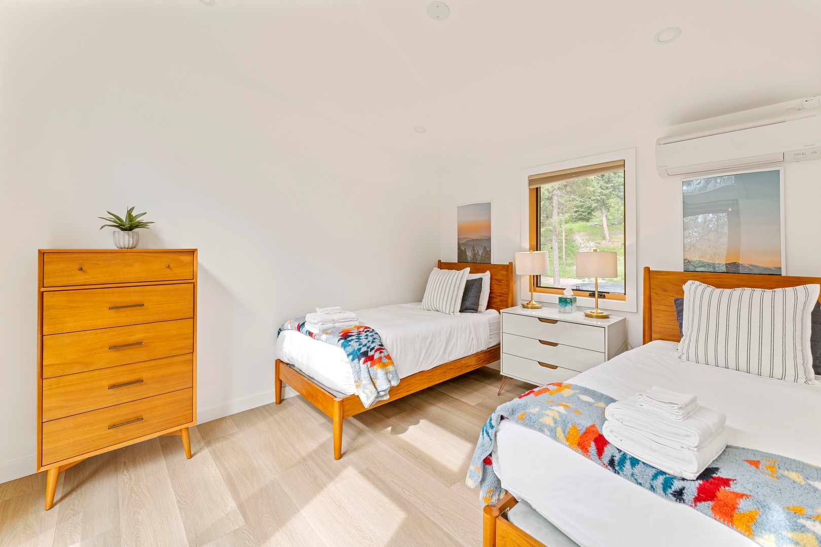 Relax in your bright twin bedroom with stylish mid-century furniture, colorful textiles, and peaceful garden views streaming through large windows.