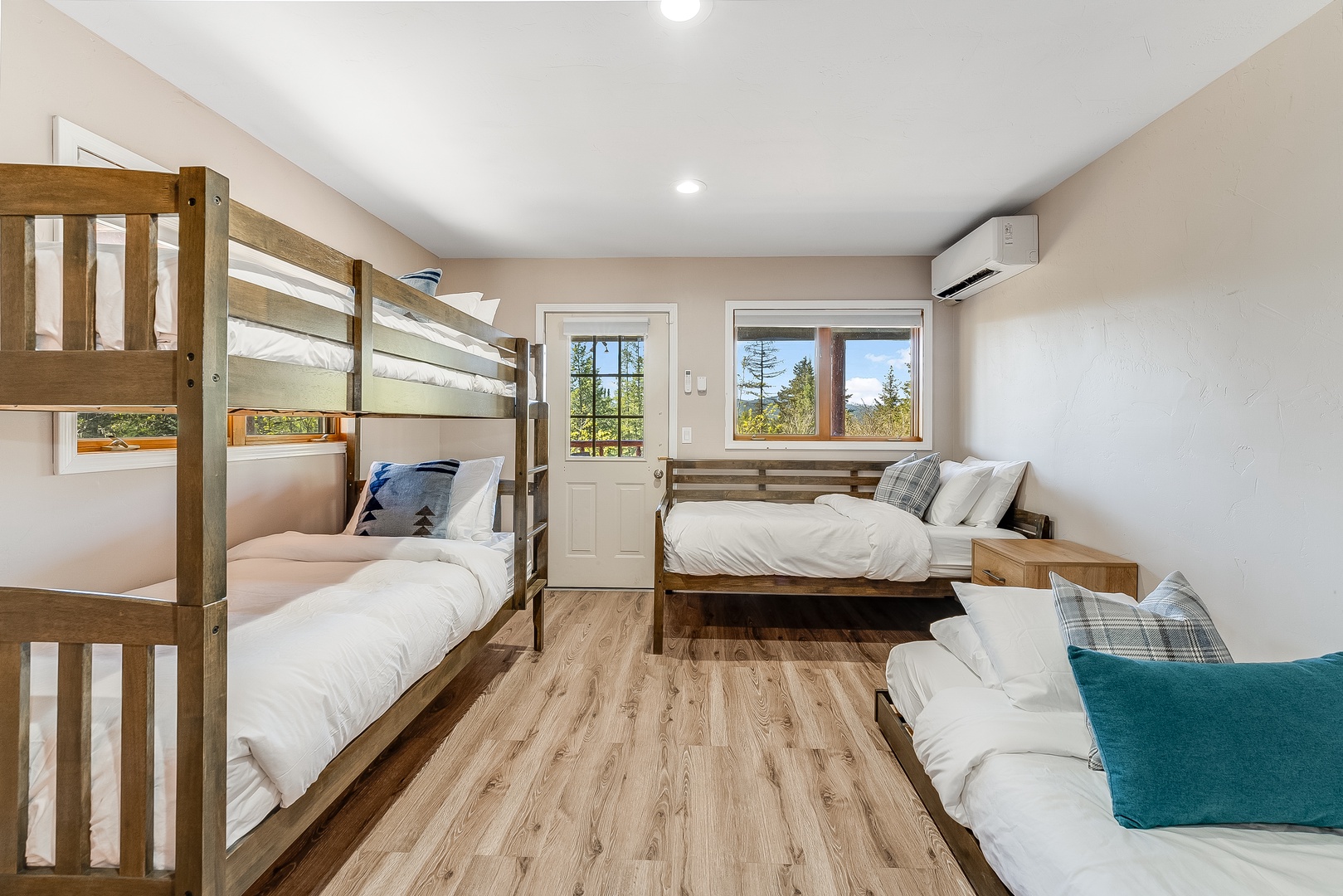 Drift off to sleep in this airy bedroom where crisp white linens and warm wood tones create a peaceful retreat. Natural light filters through large windows, framing scenic forest views beyond.