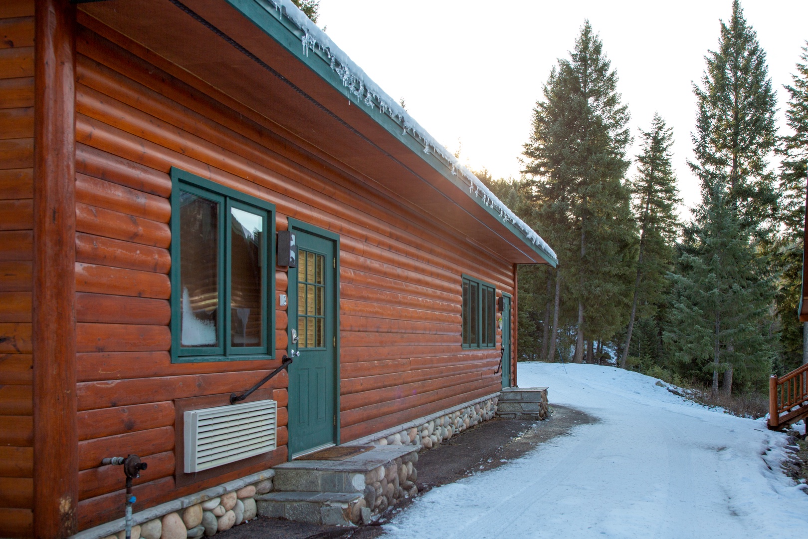 A charming log cabin nestled among towering evergreens, with warm wood tones and green accents welcoming guests to their mountain retreat.