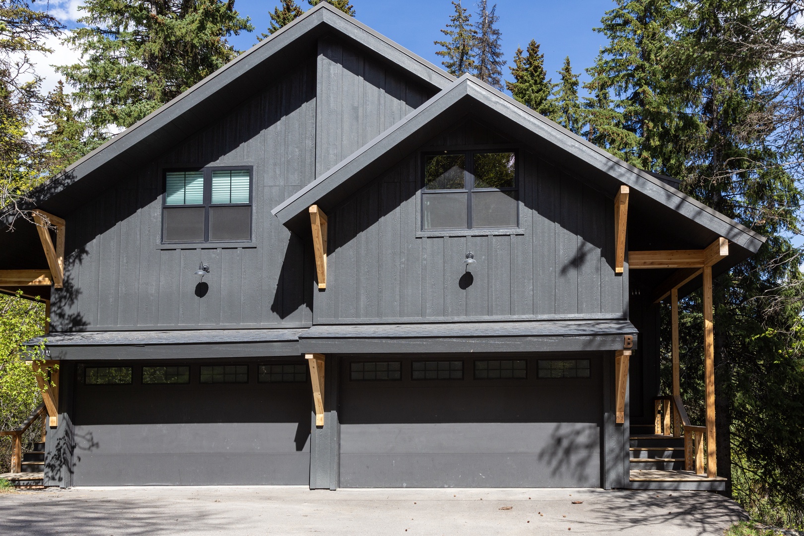 Modern mountain chalet featuring distinctive gray siding and natural wood accents, nestled among towering evergreens in a serene forest setting.