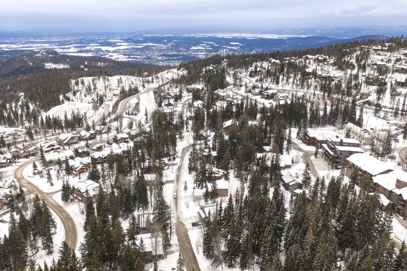 Aerial winter view of a snow-covered mountain village nestled among dense evergreen forests.