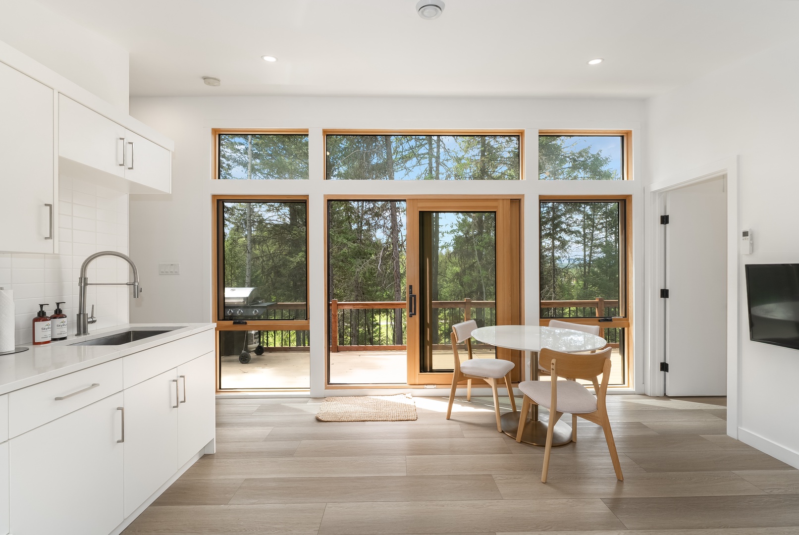 Step into your bright modern kitchen where floor-to-ceiling glass doors frame stunning forest views. Enjoy morning coffee at the cozy dining nook, then step outside to your private deck surrounded by nature.