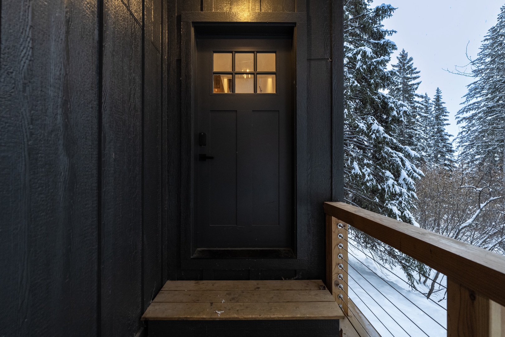 Winter wonderland entrance with snow-covered evergreens surrounding this mountain cabin's welcoming front door.