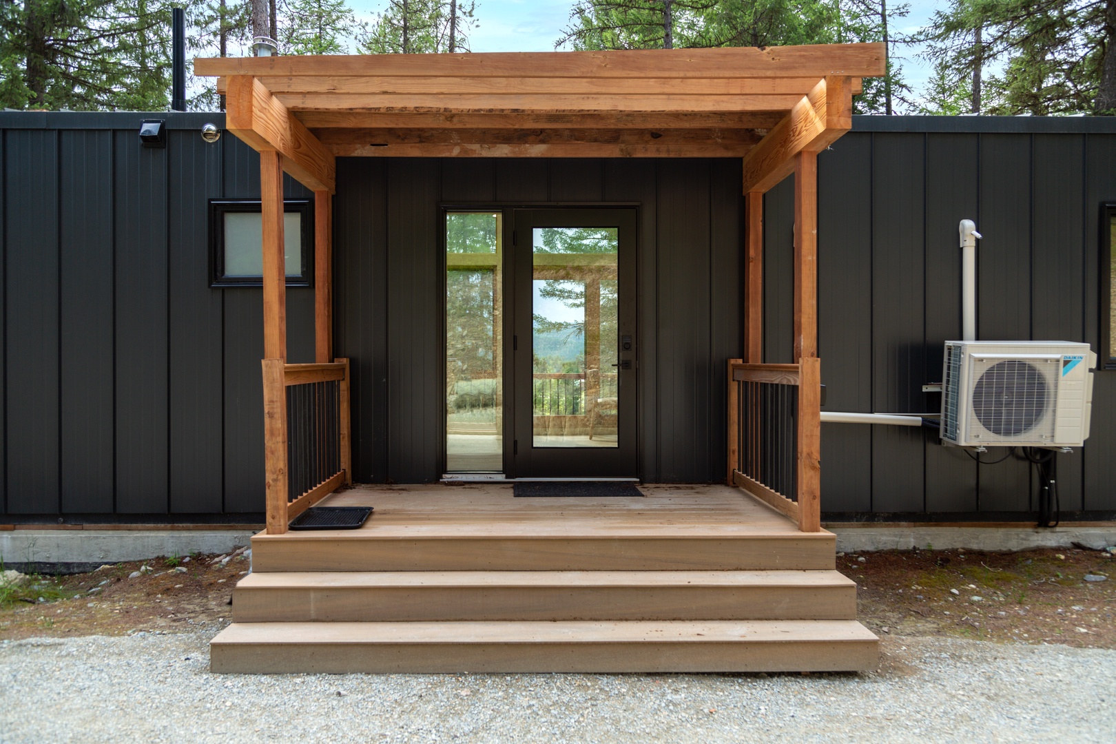 Modern cabin featuring sleek black exterior with warm cedar accents and large glass doors revealing forest views.