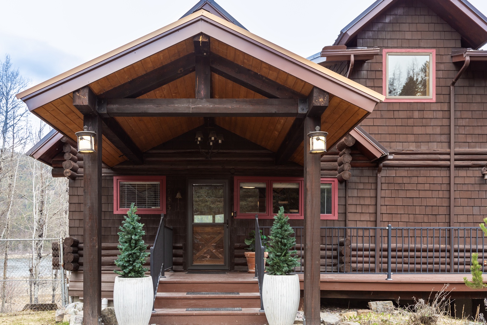 Mountain lodge entrance featuring timber frame architecture, welcoming covered entry, and evergreen planters creating a rustic alpine arrival experience.