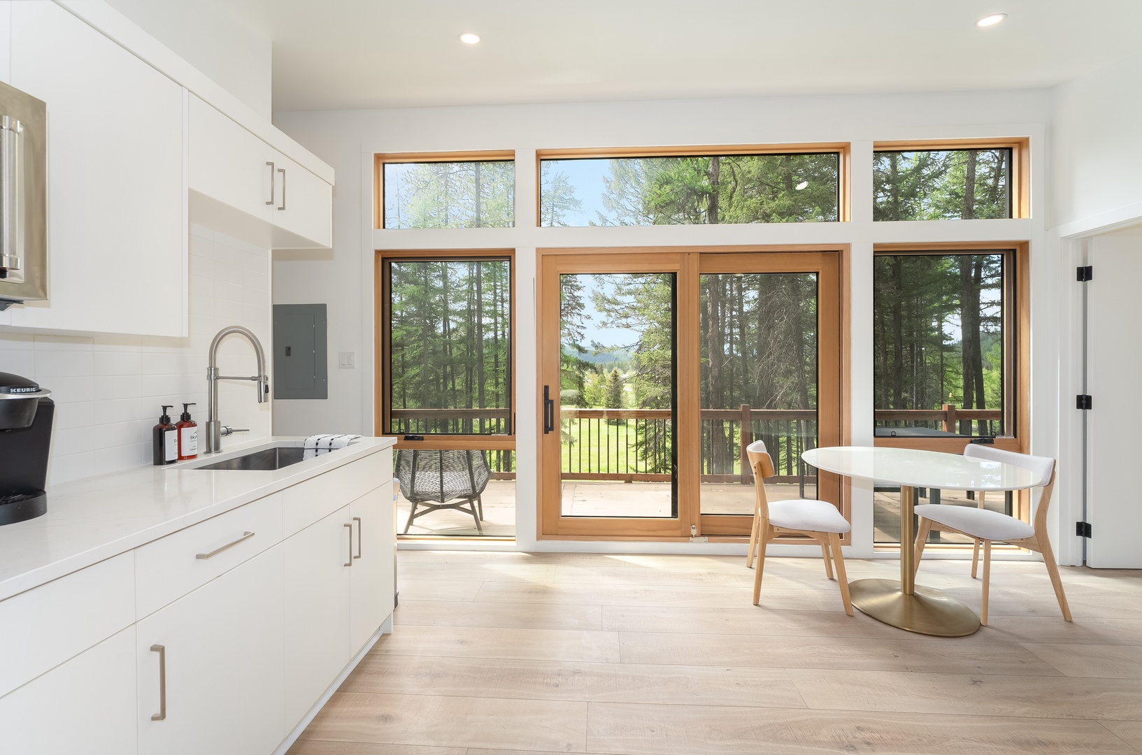 Enjoy your morning coffee at this sunlit dining nook, where floor-to-ceiling windows frame peaceful forest and meadow views from the heart of your vacation retreat.