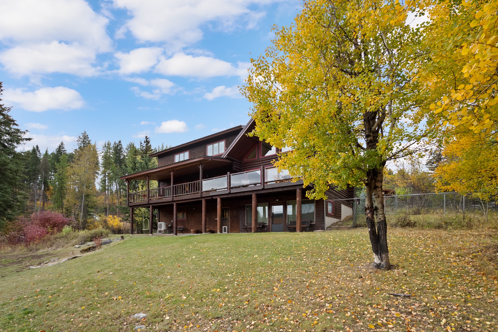 Rustic wooden lodge surrounded by golden autumn foliage and evergreen forests, featuring spacious decks and panoramic mountain views.