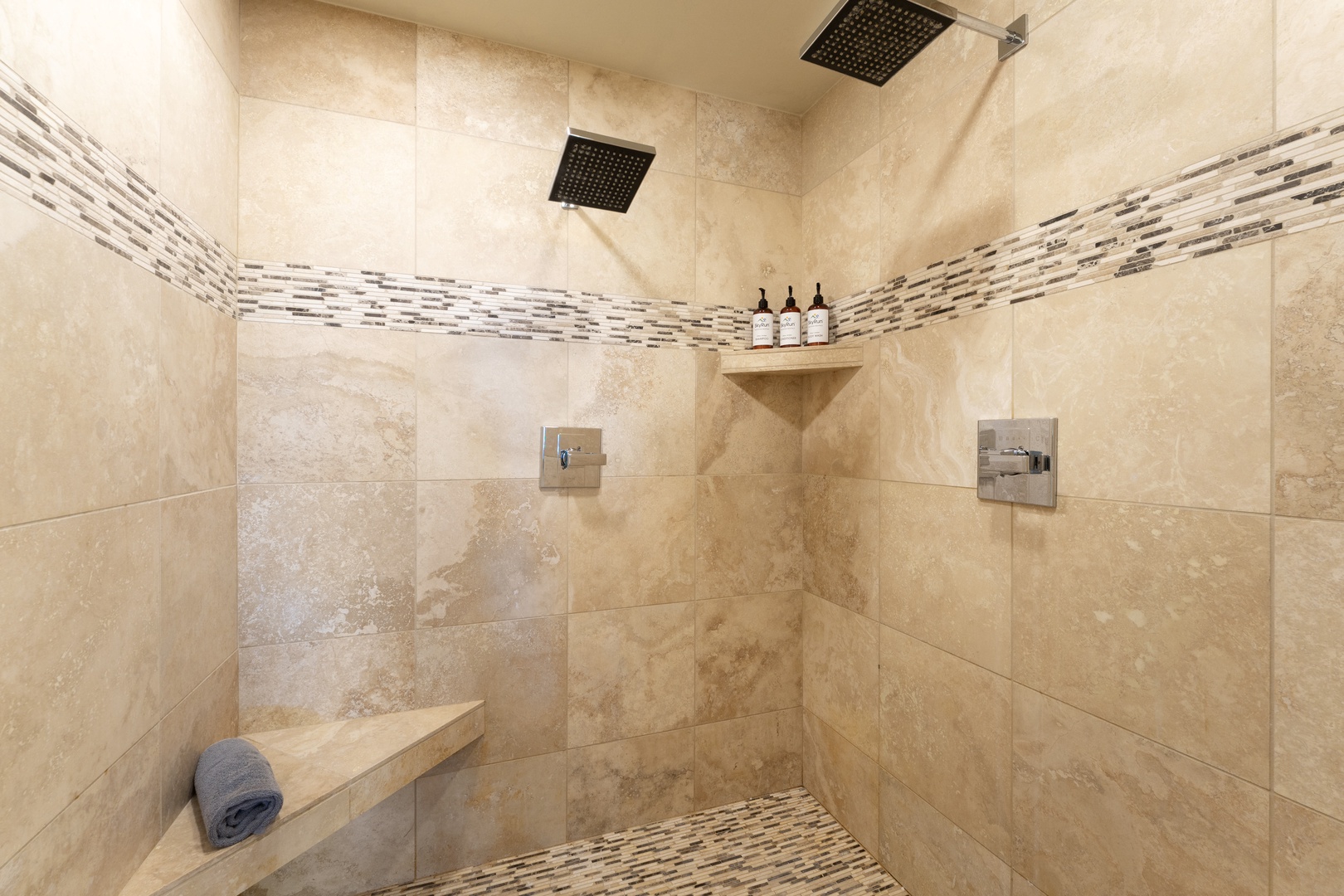 Dual rainfall showerheads invite you to unwind in this spacious walk-in shower, complete with a built-in bench and luxe tile detailing.